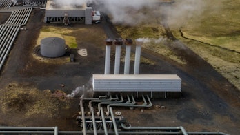 Photo depicts Hellisheidi geothermal powerplant shot from the air in early june, pipes and steam visible