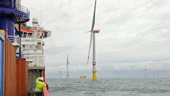 the Photo depicts a Technician standing on transfer vessel deck in the morning and looking on offshore wind farm and offshore platform around